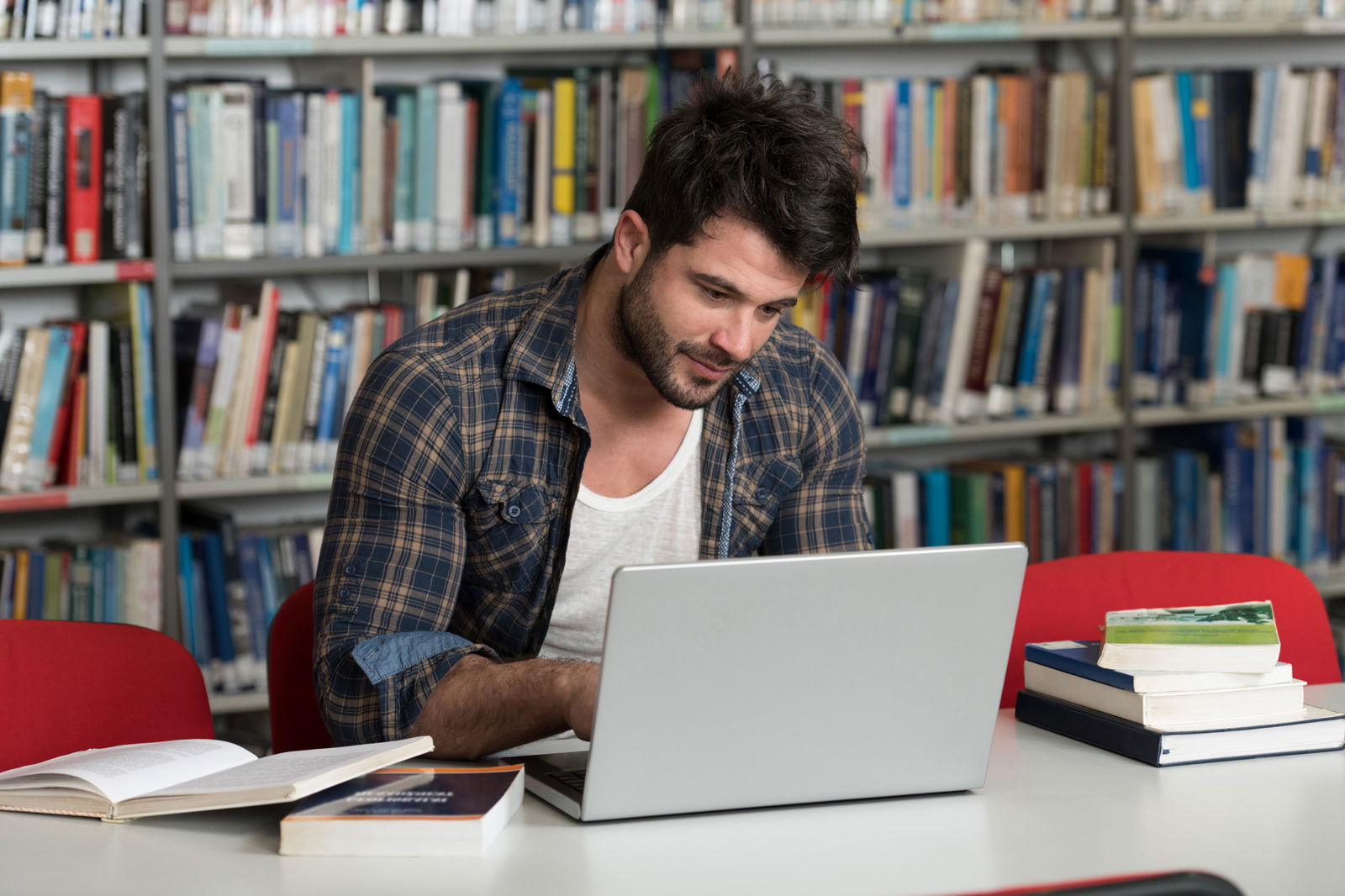 Student w okularach pisze pracę inżynierską na laptopie otoczony schematami i książkami inżynierskimi