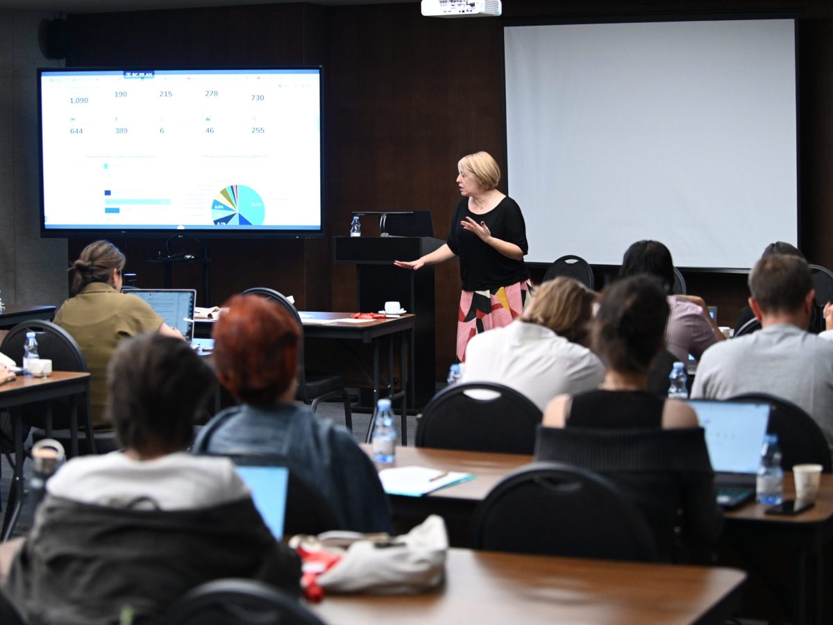 grupa studentów dyskutuje przy stole z laptopami i notatnikami w bibliotece